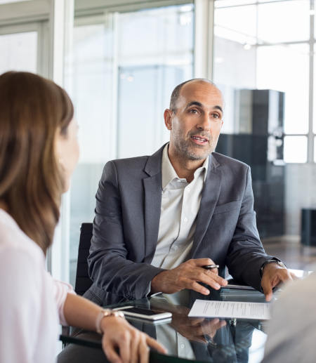 Mature financial agent showing new investment to young couple. Happy financial advisor discussing with a couple their mortgage loan. Happy couple consulting their bank agent about savings plan.