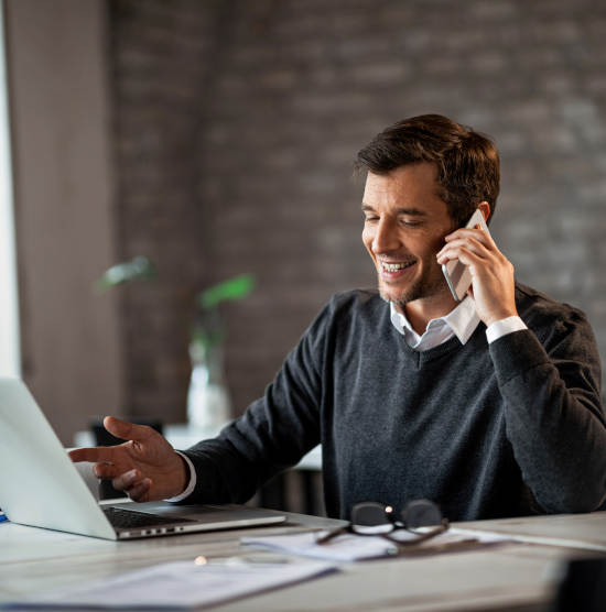 Happy businessman communicating over mobile phone and working on laptop while being at work.